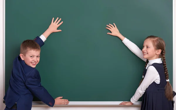 Grundschuljunge und -mädchen legen Hände auf Kreidegrund und zeigen Leerstellen, bekleidet mit klassisch schwarzem Anzug, Gruppenschülerin, Bildungskonzept — Stockfoto