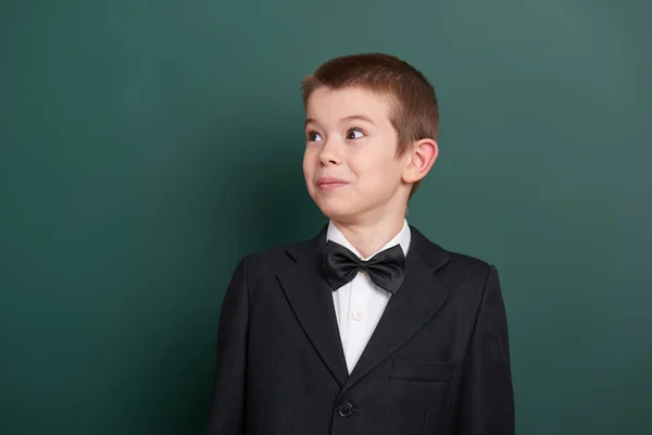 Surpised school boy portrait near green blank chalkboard background, dressed in classic black suit, one pupil, education concept — Stock Photo, Image