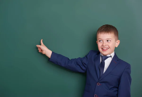 Chico de la escuela señalar el dedo cerca de fondo pizarra en blanco, vestido con traje negro clásico, alumno de grupo, concepto de educación — Foto de Stock