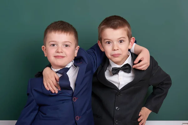 Two friends, elementary school boy near blank chalkboard background, dressed in classic black suit, group pupil, education concept — Stock Photo, Image