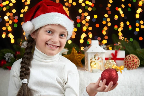 Retrato da menina criança com decoração de Natal, fundo escuro com luzes, expressão facial e emoções felizes, vestida com chapéu de santa, conceito de férias de inverno — Fotografia de Stock