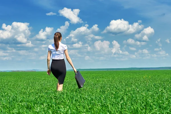 Mujer de negocios caminar en campo de hierba verde al aire libre. Hermosa joven vestida de traje, paisaje de primavera, día soleado brillante — Foto de Stock