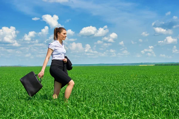 Mujer de negocios caminar en campo de hierba verde al aire libre. Hermosa joven vestida de traje, paisaje de primavera, día soleado brillante — Foto de Stock