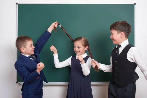 Child play and having fun, boys pull the girl braids, near blank school chalkboard background, dressed in classic black suit, group pupil, education concept — Stock Photo, Image