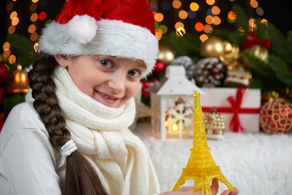Dítě dívka portrét s Eiffelovkou a vánoční dekorace, tmavé pozadí s světla, výraz obličeje a šťastný emoce, oblečený v santa čepice, Zimní dovolená concept — Stock fotografie