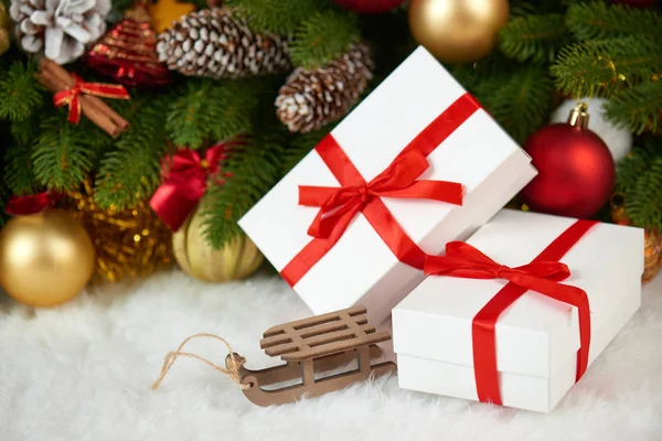 Christmas decoration on fir tree branch closeup, wooden sledge toy, gifts, xmas ball, cone and other object on white blank space fur, holiday concept, place for text — Stock Photo, Image