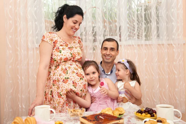 family drinking tea in dining room, pregnant woman