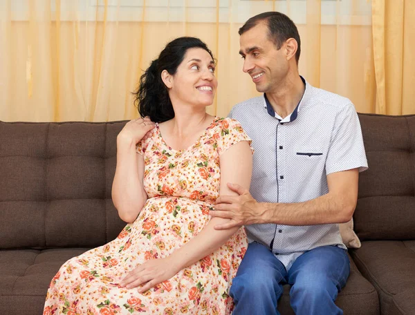 Casal feliz interior, mulher grávida e homem, pessoas bonitas retrato, sente-se no sofá — Fotografia de Stock