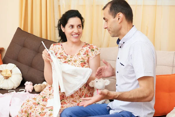 Parents choose clothes for the newborn baby. pregnant woman and man. happy couple sitting on the couch at home — Stock Photo, Image