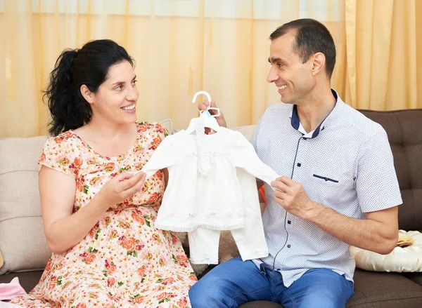 Parents choose clothes for the newborn baby. pregnant woman and man. happy couple sitting on the couch at home — Stock Photo, Image