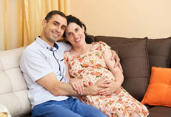 Zwangere vrouw en man indoor portret, gelukkige mensen zitten op de Bank — Stockfoto