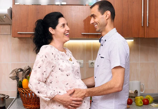 W ciąży kobieta i mężczyzna w aranżacji kuchni z świeże owoce i warzywa, zdrowe jedzenie koncepcja, szczęśliwa para — Zdjęcie stockowe