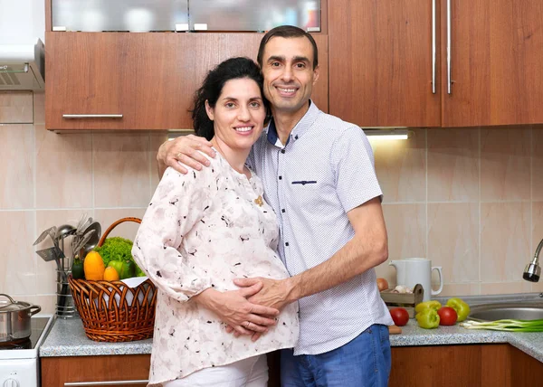 Mulher grávida e homem na cozinha interior com frutas e legumes frescos, conceito de comida saudável, casal feliz — Fotografia de Stock