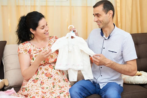 Parents choose clothes for the newborn baby. pregnant woman and man. happy couple sitting on the couch at home — Stock Photo, Image