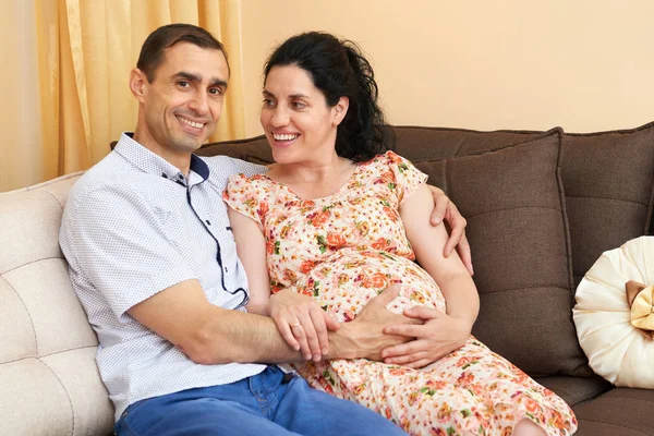 Zwangere vrouw en man indoor portret, gelukkige mensen zitten op de Bank — Stockfoto