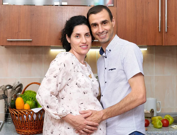 Mulher grávida e homem na cozinha interior com frutas e legumes frescos, conceito de comida saudável, casal feliz — Fotografia de Stock