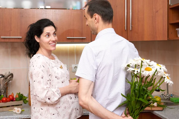 Bărbatul dă flori femeii însărcinate, cuplului în interiorul bucătăriei cu fructe și legume proaspete, concept alimentar sănătos — Fotografie, imagine de stoc