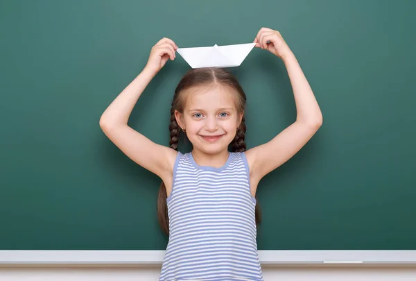 Pupil with origami ship posing at school board, empty space, education concept — Stock Photo, Image