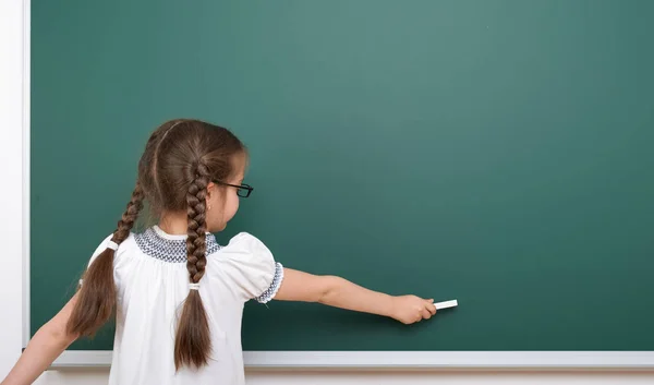 Schoolmeisje schrijven krijt op een bord, lege ruimte, onderwijs concept — Stockfoto