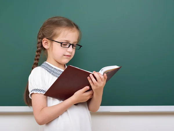 Chica de la escuela leer libro, posando en la junta escolar, espacio vacío, concepto de educación —  Fotos de Stock