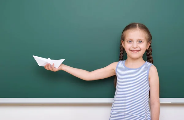 Pupil with origami ship posing at school board, empty space, education concept — Stock Photo, Image