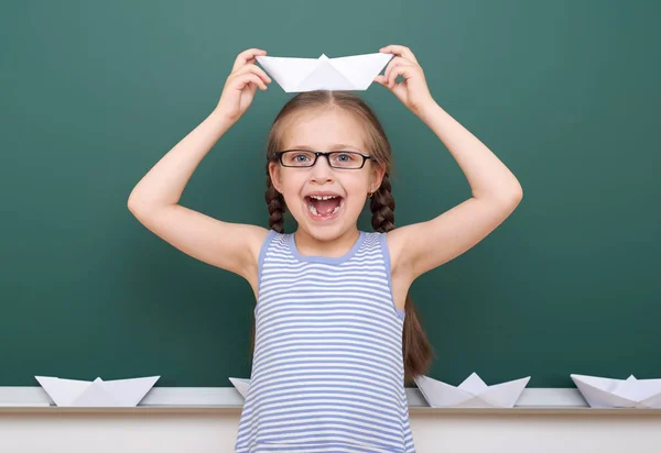 Colegiala con barco de papel jugar cerca de una pizarra, espacio vacío, concepto de educación — Foto de Stock