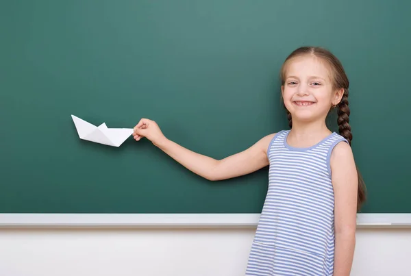 Pupil with origami ship posing at school board, empty space, education concept — Stock Photo, Image