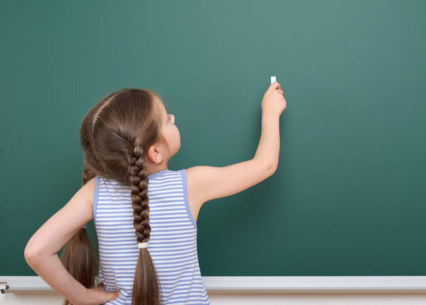 Schoolgirl writing chalk on a blackboard, empty space, education concept
