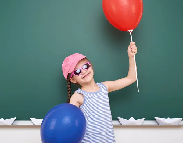 Schoolgirl with paper boat and balloon play near a blackboard, empty space, education concept — Stock Photo, Image