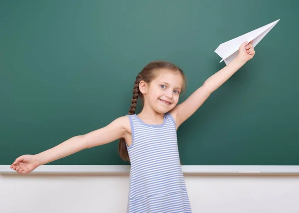 Colegiala con avión de papel jugar cerca de una pizarra, espacio vacío, concepto de educación — Foto de Stock