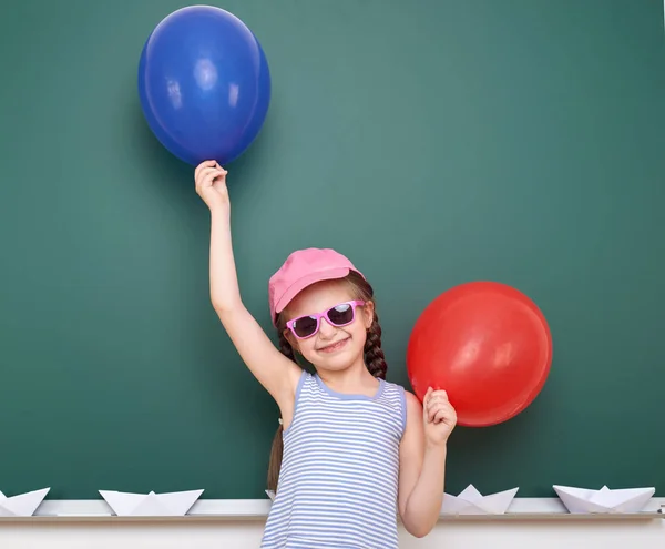Schoolgirl with paper boat and balloon play near a blackboard, empty space, education concept — Stock Photo, Image