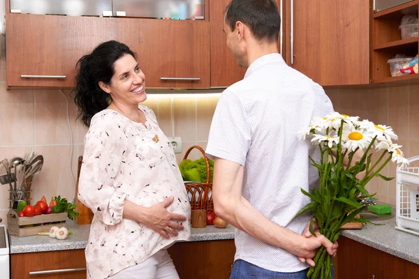 Muž dává heřmánek květiny na těhotnou ženu, pár v interiéru kuchyně s čerstvého ovoce a zeleniny, zdravé jídlo koncept — Stock fotografie