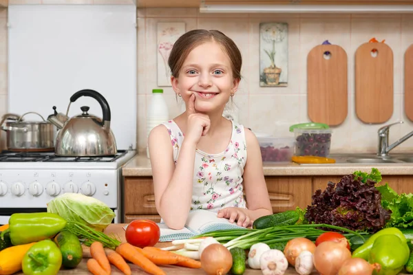 Child girl with fruits and vegetables in home kitchen interior, read cooking book, healthy food concept — Stock Photo, Image