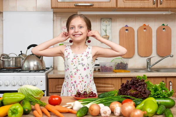 Criança menina brincar e se divertir com cerejas, frutas e legumes em casa cozinha interior, conceito de comida saudável — Fotografia de Stock