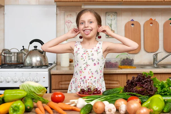 Criança menina brincar e se divertir com cerejas, frutas e legumes em casa cozinha interior, conceito de comida saudável — Fotografia de Stock