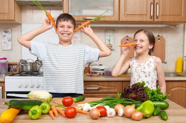 Çocuk kız ve erkek domates ve havuç ile eğleniyor. Meyve ve sebze ile ev mutfak iç. Sağlıklı gıda kavramı