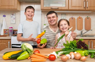 Baba ve iki çocuk ev mutfak iç. Mutlu aile, kız ve erkek meyve ve sebze ile eğleniyor. Sağlıklı gıda kavramı.