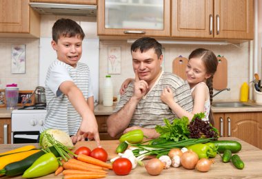 Baba ve iki çocuk ev mutfak iç. Mutlu aile, kız ve erkek meyve ve sebze ile eğleniyor. Sağlıklı gıda kavramı.