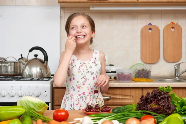 Child girl eat cherries, fruits and vegetables in home kitchen i — Stock Photo, Image
