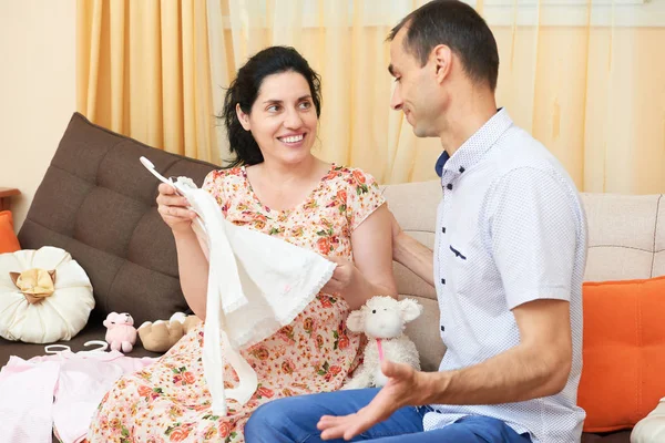 Parents choose clothes for the newborn baby. pregnant woman and man. happy couple sitting on the couch at home — Stock Photo, Image