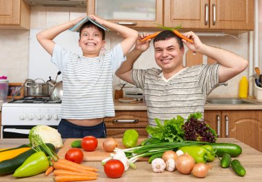 Baba ve oğul pişirme ve ev mutfak iç sebze ile eğleniyor. İki kişi, erkek ve çocuk. Meyve ve sebze. Sağlıklı gıda kavramı