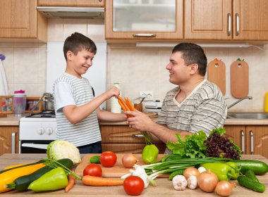 Baba ve oğul pişirme ve ev mutfak iç sebze ile eğleniyor. İki kişi, erkek ve çocuk. Meyve ve sebze. Sağlıklı gıda kavramı
