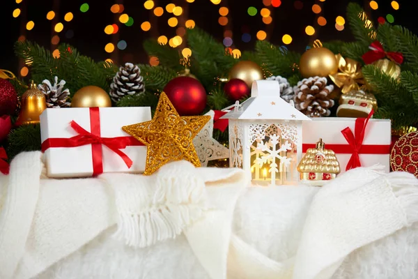 Kerstdecoratie op wit bont met fir tree branch close-up, geschenken, xmas bal, kegel en andere objecten op een donkere achtergrond met lichten, concept van winter vakantie — Stockfoto
