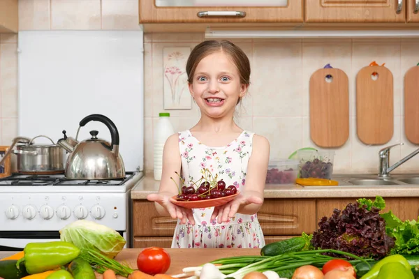 Girl giving a plate of cherries. Many fruits and vegetables on t — Stock Photo, Image