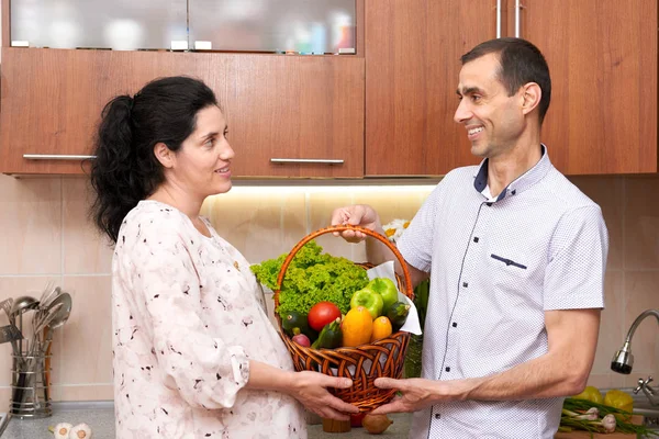 couple in kitchen interior with basket of fresh fruits and vegetables, healthy food concept, pregnant woman and man