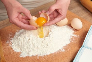 Kadın un bir ahşap arka plan üzerinde pişirme için hazırlanıyor. Çiğ gıda ve mutfak aletleri. El ve gıda portre. Hamur yemek yumurta kırmak.