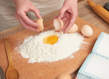 Kadın un bir ahşap arka plan üzerinde pişirme için hazırlanıyor. Çiğ gıda ve mutfak aletleri. El ve gıda portre. Hamur yemek yumurta kırmak.