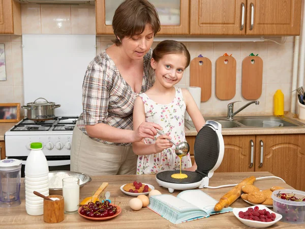 Woman and child girl baking waffles in home kitchen. Raw food and fruits. Healthy food concept.