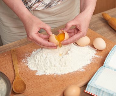 Kadın un bir ahşap arka plan üzerinde pişirme için hazırlanıyor. Çiğ gıda ve mutfak aletleri. El ve gıda portre. Hamur yemek yumurta kırmak.