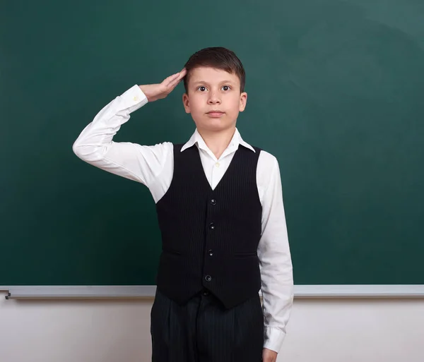 School boy gesturing a military salute, portrait near green blank chalkboard background, dressed in classic suit, one pupil, education concept — Stock Photo, Image